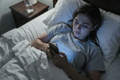 Femme fatiguée dans son lit consultant son smartphone la nuit, illustrant le lien entre écrans et troubles du sommeil
